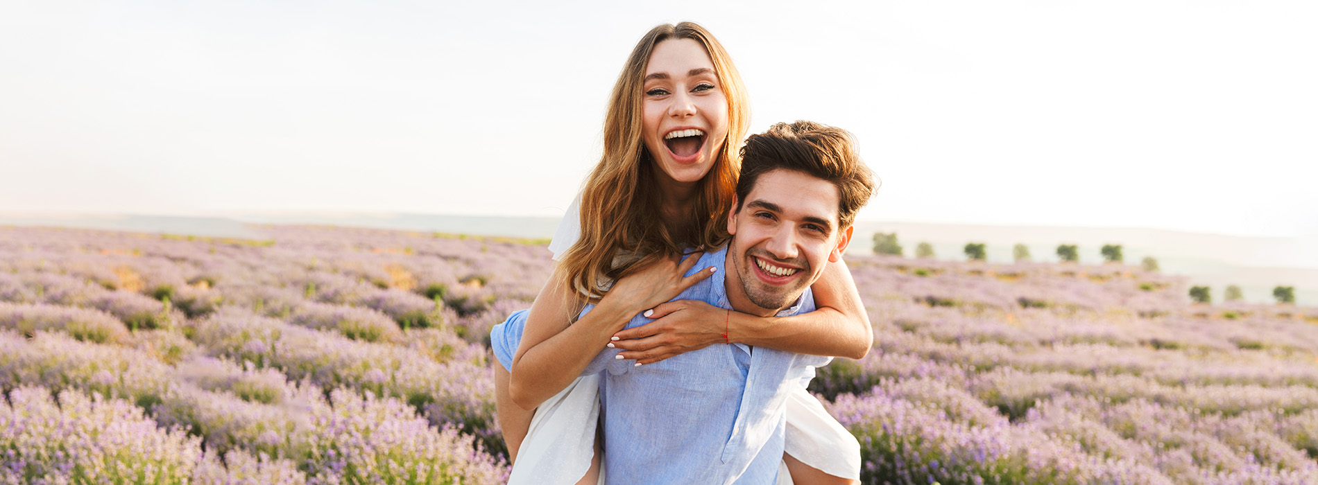 Two people, likely a couple, embracing and smiling at the camera in a field with lavender plants.