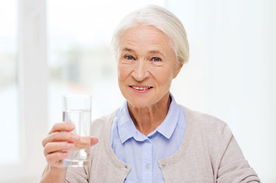 The image shows a woman holding a glass of water, smiling and looking directly at the camera.